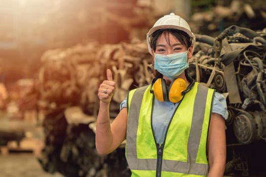 Asian women worker thumbs up waring face mask happy working safety work in a heavy industrial factory with engine machine background