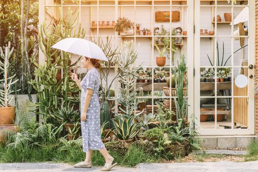 Asian women walking leisure around with nature garden cactus nursery plant shop in summer season with umbrella.