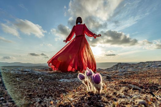 Rise of the mystic. sunset over the clouds with a girl in a long red dress. There is a dream grass in the meadow with purple flowers