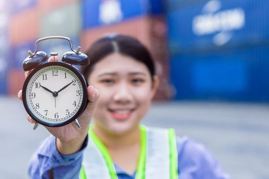 happy smile women worker working at port cargo shipping hand holding alarm clock for good times fast in time shipping concept.