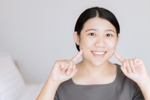 Beautiful young Asian woman white baby face healthy teeth look finger point at face for facial skin care concept.