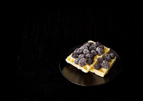 Belgian wafers with frozen blackberries on a black background.