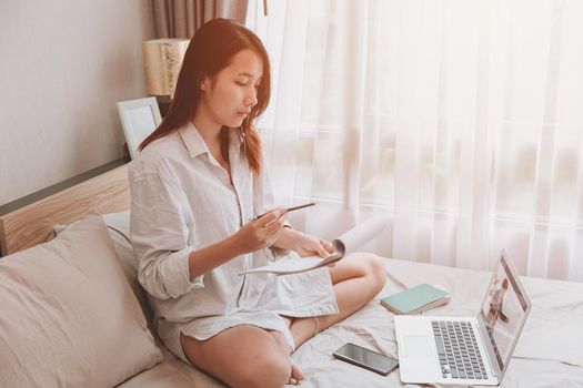 Woman stay at home using laptop for online education learning during self quarantine on the bed.