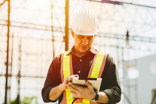 Foreman builder engineer worker using tablet computer to check building floor plan at construction site.