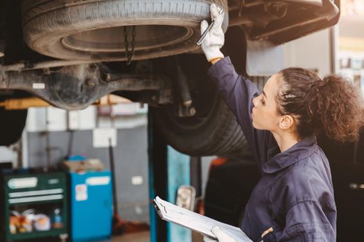 Woman garage worker maintenance checklist at automobile service center, Female in auto mechanic car technician work service check and repair customer car, inspecting car under hood