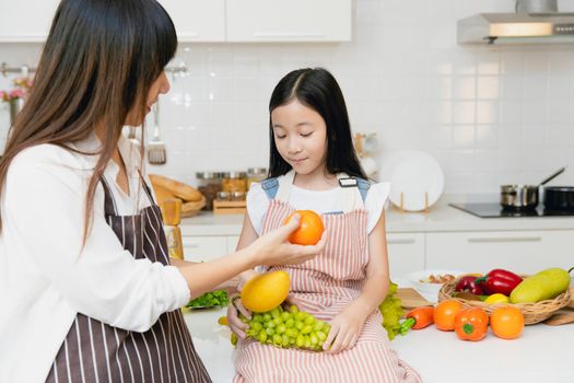 Mother teaching child to eating fruit and advise to eat orange for vitamin C and healthy food.