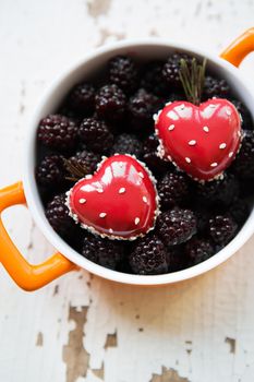 A full blackberry plate with a dessert in the form of a heart stands on a wooden background, close-up.