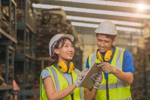 Asian young man and women worker team engineer working help support together using tablet happy smile to work in factory industry.