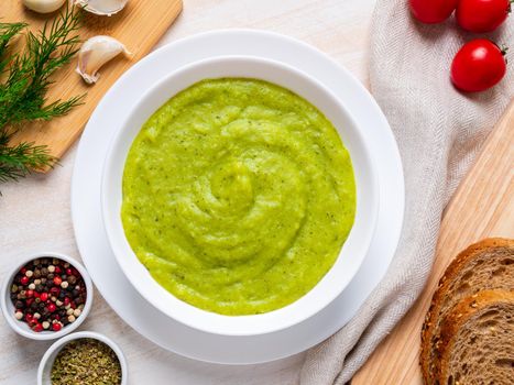 large white bowl with vegetable green cream soup of broccoli, zucchini, green peas on white background, top view.