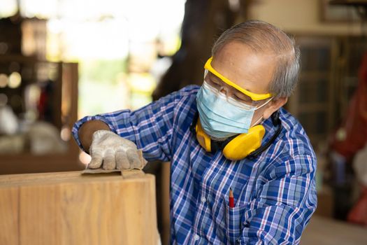 Elder worker wood woodcraft retire hobby for good retirement, Asian male mature professional master of making wooden furniture with face mask protective.