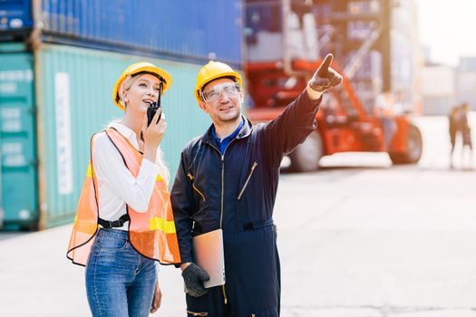 logistic worker man and woman working team with radio control loading containers at port cargo to trucks for export and import goods.