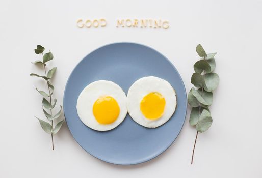 two eggs on a plate with a sprig of eucalyptus, an inscription good morning