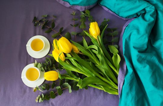 Yellow tulips and two cups of tea in bed, morning