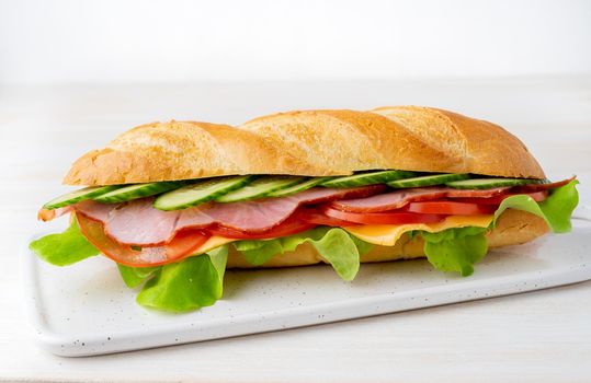 sandwich with ham, cheese, tomatoes, cucumbers, lettuce on white background