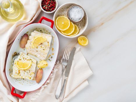 cod fish fillet, freshly cooked in oven with onion in red porcelain dish for baking, lemon, top view, copy space.