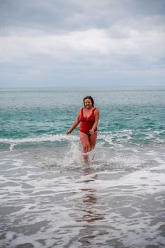 Woman in a bathing suit at the sea. A fat young woman in a red swimsuit enters the water during the surf.