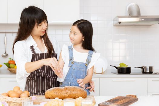 Mother and her child girl cooking food in home kitchen. Kid baking home made bread bun happy together with mom for holiday activity.