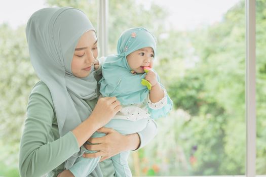 Muslim Mother with her baby. Islamic Asian women wearing hijab holding support child infant indoor at home.