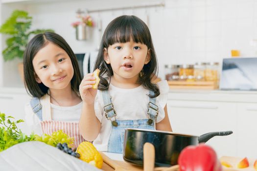 Portrait two Asian sister playing and care together eating at home kitchen.