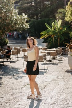 Girl tourist walking through ancient narrow street on a beautiful summer day in MEDITERRANEAN MEDIEVAL CITY , OLD TOWN bUDVA, MONTENEGRO. Young beautiful cheerful woman walking on old street at tropical town. Pretty girl looking at you and smiling