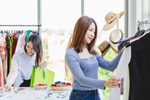 Women customer choosing clothes looking for new shirt in fashion shop with friend happy smile.