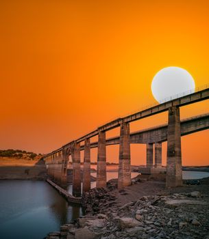 Drought with three bridges on different levels and huge sun over orange sky for text space