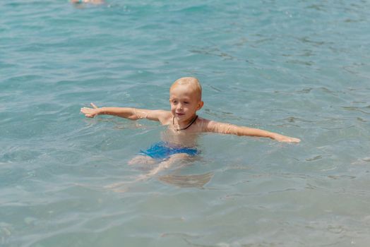 Child learning to swim in the open sea of tropical resort. Kids learn swimming. Exercise and training for young children. Little boy with colorful float board in sport club. Swimming baby or toddler. Happy child boy swims in sea in swimming circle with splash. Blue sky and water. Swimming training. Fun joy activities on vacation in the beach. Childhood moments lifestyle. Freedom careless. boy swim in the sea.