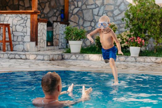 Excited boy in googles jumping in water from shoulders of his father standing in swimming pool