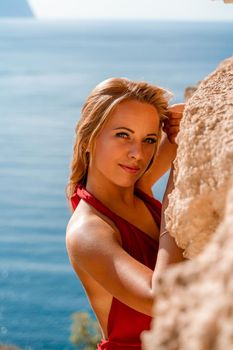 Smiling young woman in a red dress looks at the camera. A beautiful tanned girl enjoys her summer holidays at the sea. Portrait of a stylish carefree woman laughing at the ocean