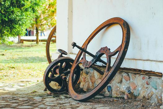 Steel old rusty wheel from agricultural machinery near white wall. High quality photo