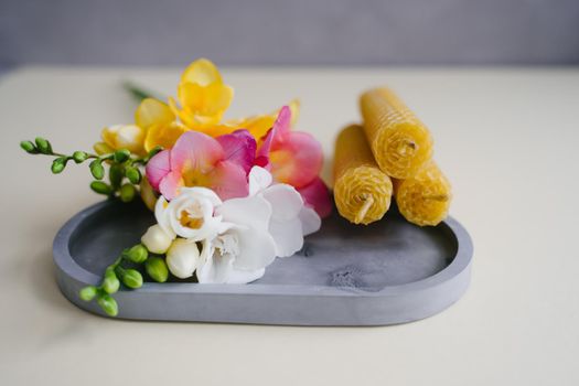 A set of three honey candles on a plaster tray with a bouquet of fragrant freesias.