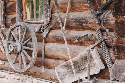 Old remnants of agricultural utensils hang on a wall of logs. High quality photo