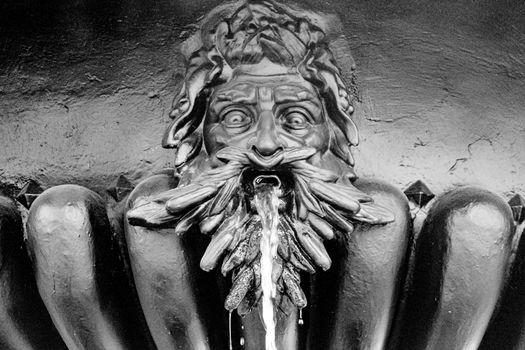 Fountain with a statue of a man's head, water flows from his mouth. High quality photo