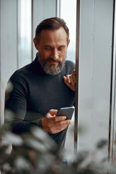 Caucasian bearded man standing near window while reading the message
