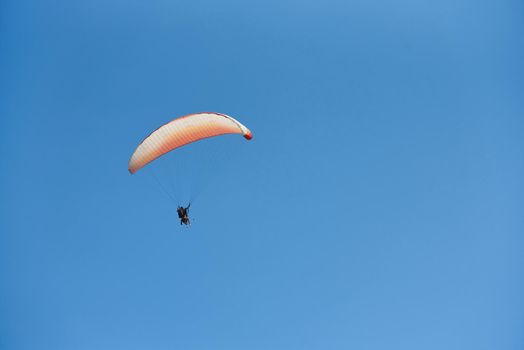 Paragliding with two people against blue sky.
