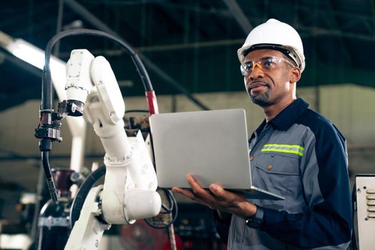 African American factory worker working with adept robotic arm in a workshop . Industry robot programming software for automated manufacturing technology .