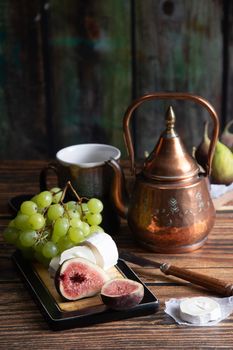 cheese plate with goat cheese, grapes and figs, copper teapot, angle view, healthy food, high-calorie breakfast. High quality photo