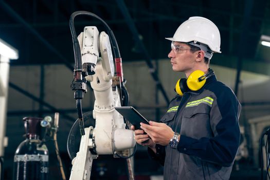 Young factory worker working with adept robotic arm in a workshop . Industry robot programming software for automated manufacturing technology .