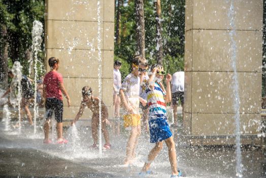 Kyiv, Ukraine - August 01, 2021: Boys jumping in water fountains. Children playing with a city fountain on hot summer day. Happy friends having fun in fountain. Summer weather. Friendship, lifestyle and vacation.