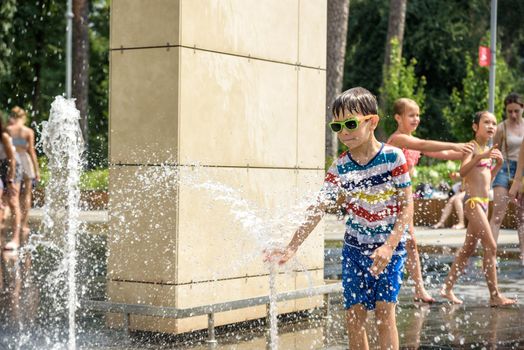 Kyiv, Ukraine - August 01, 2021: Boys jumping in water fountains. Children playing with a city fountain on hot summer day. Happy friends having fun in fountain. Summer weather. Friendship, lifestyle and vacation.