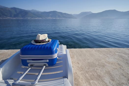 Blue suitcase on a sun lounger on the shore of the adriatic sea in Montenegro, travel concept.