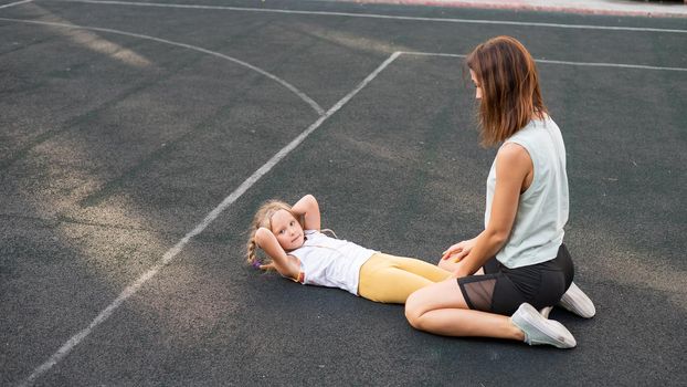 Mother and daughter go in for sports outdoors. Caucasian woman and little girl are engaged in fitness at the stadium