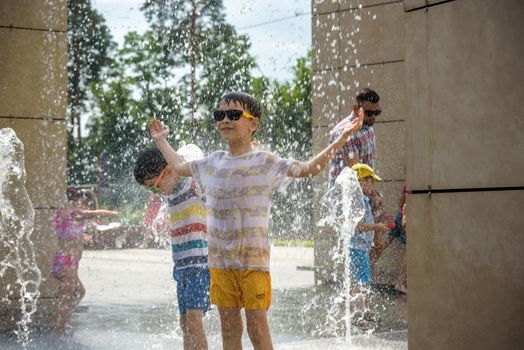 Kyiv, Ukraine - August 01, 2021: Boys jumping in water fountains. Children playing with a city fountain on hot summer day. Happy friends having fun in fountain. Summer weather. Friendship, lifestyle and vacation.