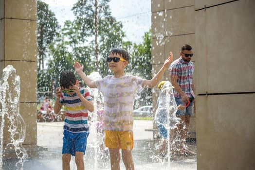 Kyiv, Ukraine - August 01, 2021: Boys jumping in water fountains. Children playing with a city fountain on hot summer day. Happy friends having fun in fountain. Summer weather. Friendship, lifestyle and vacation.