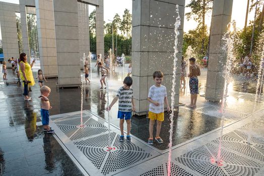 Kyiv, Ukraine - August 01, 2021: Boys jumping in water fountains. Children playing with a city fountain on hot summer day. Happy friends having fun in fountain. Summer weather. Friendship, lifestyle and vacation.