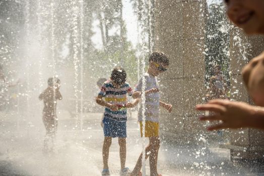 Kyiv, Ukraine - August 01, 2021: Boys jumping in water fountains. Children playing with a city fountain on hot summer day. Happy friends having fun in fountain. Summer weather. Friendship, lifestyle and vacation.