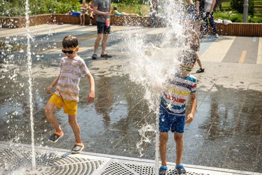 Kyiv, Ukraine - August 01, 2021: Boys jumping in water fountains. Children playing with a city fountain on hot summer day. Happy friends having fun in fountain. Summer weather. Friendship, lifestyle and vacation.