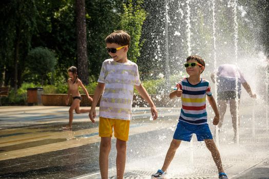 Kyiv, Ukraine - August 01, 2021: Boys jumping in water fountains. Children playing with a city fountain on hot summer day. Happy friends having fun in fountain. Summer weather. Friendship, lifestyle and vacation.