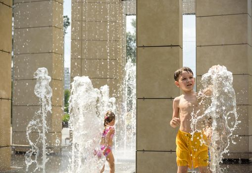 Kyiv, Ukraine - August 01, 2021: Boys jumping in water fountains. Children playing with a city fountain on hot summer day. Happy friends having fun in fountain. Summer weather. Friendship, lifestyle and vacation.