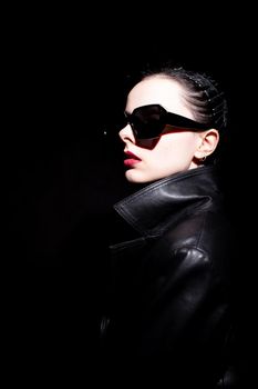 woman in leather coat and black sunglasses, black background. High quality photo